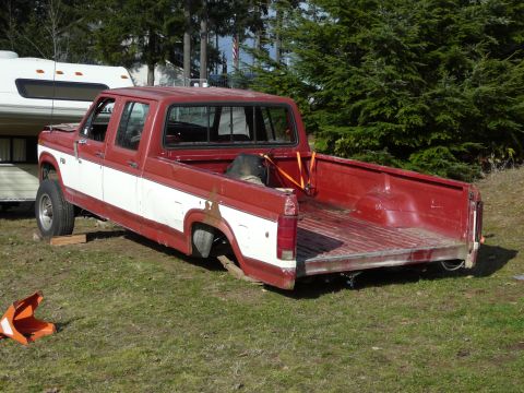 1991 Ford Bronco - A red and white pickup truck bed is shown from a rear 3/4 angle, with the truck sitting on grass. A white RV is parked behind the truck.