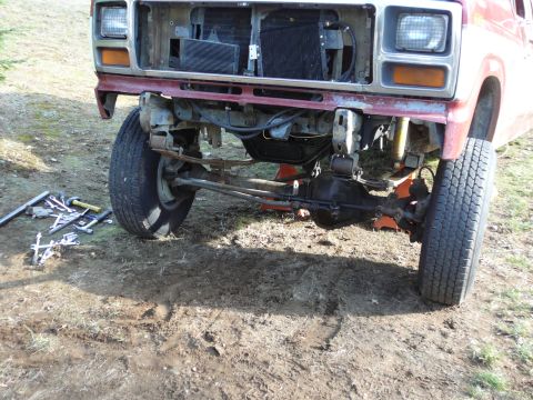 1991 Ford Bronco - The front axle and suspension of a red truck are visible, with tools scattered on the ground nearby. The vehicle appears to be undergoing m…