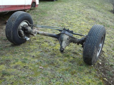 1991 Ford Bronco - A front axle assembly with two tires and wheels is shown resting on a grassy area. The axle is rusty and appears to be from an older vehicl…