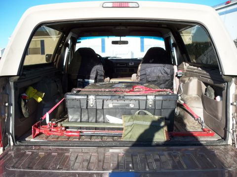 1996 Ford Bronco - View into the rear cargo area of an SUV through the open tailgate, with a big black equipment trunk on a slide-out tray.