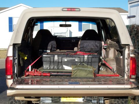 1996 Ford Bronco - Tan SUV with the rear hatch and tailgate open, showing folded rear seats and a black storage box plus gear in the cargo area.