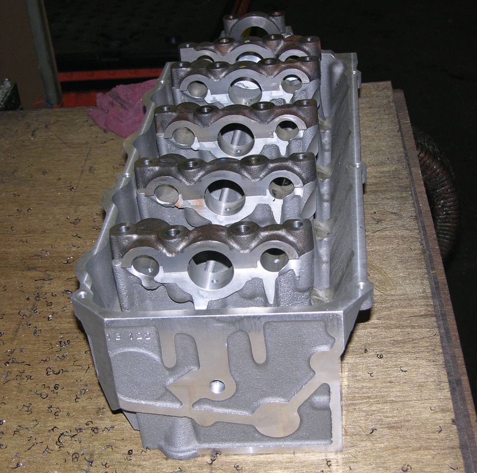 Bare aluminum cylinder head on a workbench showing machined valve seats and pushrod holes