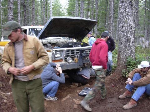 1991 Ford Bronco - Several men work on a white and yellow Ford Bronco with its hood open in a wooded area. Tools are laid out on the ground near the front of…