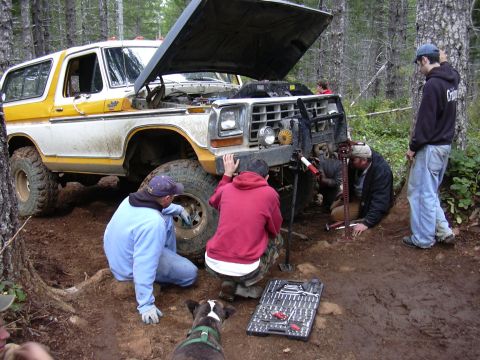 1991 Ford Bronco - A group of people are working on a white and yellow Ford Bronco, which appears to be stuck in the mud. They are using a jack and tools to t…