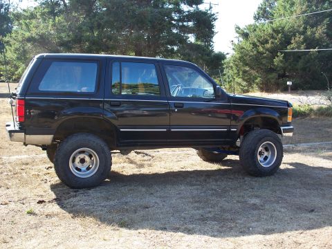 1977 Ford F-150 - A lifted black SUV is parked on a dry, grassy area with trees in the background. The vehicle has large tires and appears to be a Ford Explo…