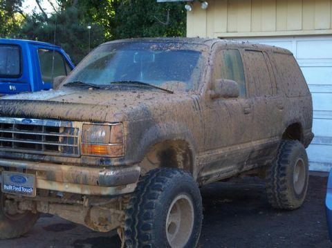 1977 Ford F-150 - A mud-covered Ford Explorer is parked in front of a garage. A blue pickup truck is partially visible to the left of the Ford.