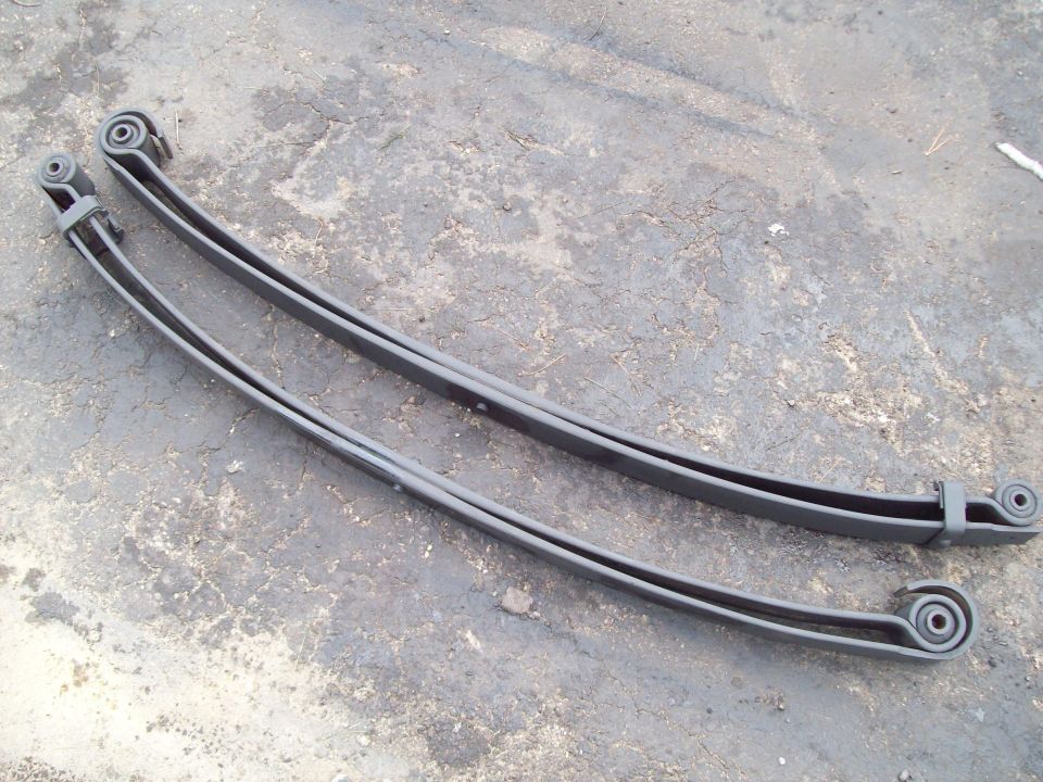 Two gray-painted leaf springs with eyelet ends lying on cracked concrete