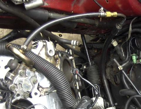 1997 Ford Taurus - A close-up view of engine components and hoses in a vehicle's engine bay. A black ribbed hose connects to a brass fitting on a metal line,…
