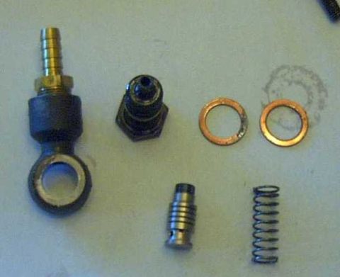 1997 Ford Taurus - A collection of disassembled parts, including a brass barbed fitting, a black hex fitting, two copper washers, a small metal cylinder, and…