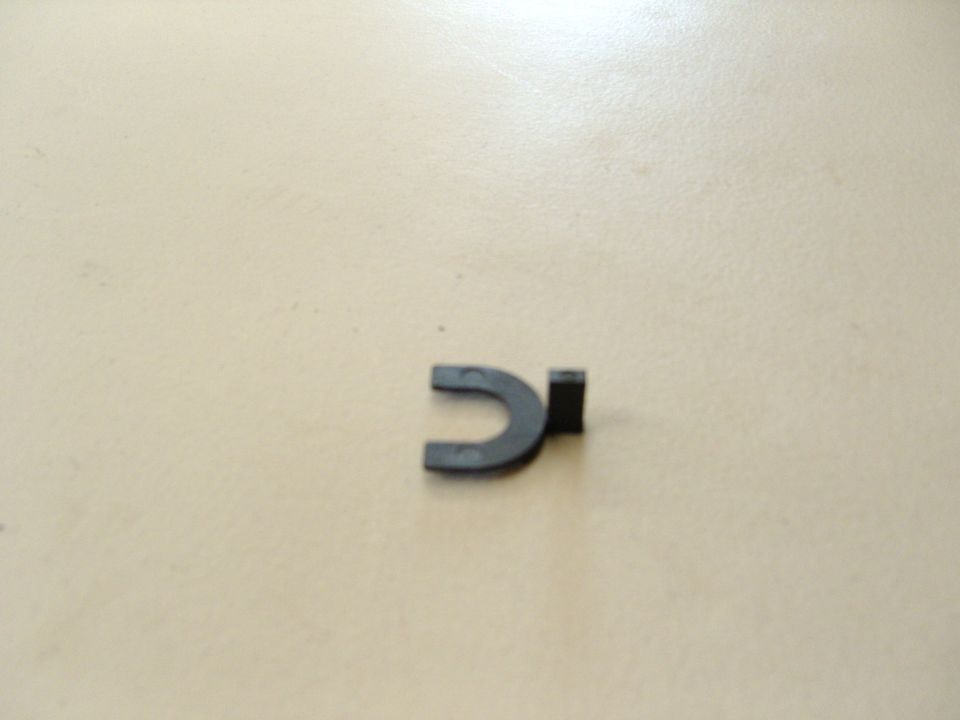 Photo of a small black plastic U-shaped retaining clip on a tan surface