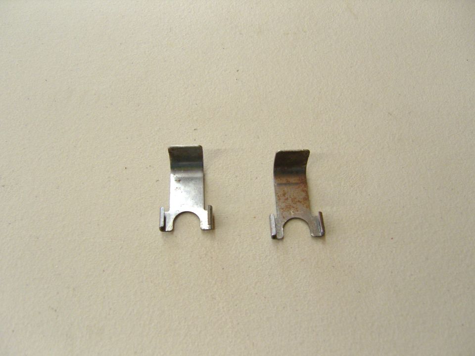 Photo of two small bent metal retaining clips on a tan surface