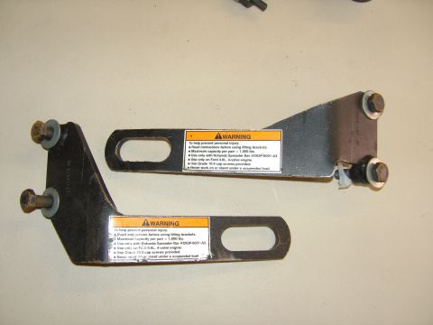 2007 Ford Mustang - Photograph of two metal engine lifting brackets bearing orange warning instruction labels, not a standalone document.