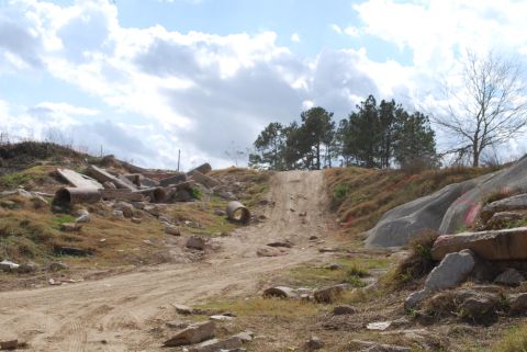 2008 Jeep Wrangler - A dirt path winds through a rocky, debris-strewn landscape under a cloudy sky. Piles of concrete rubble and large concrete pipes are scatte…