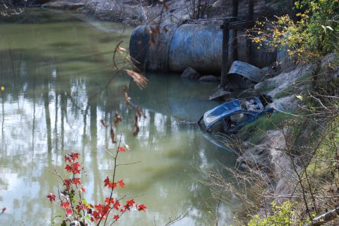 2008 Jeep Wrangler - A blue car is submerged in murky water next to a large corrugated metal pipe. The car appears to be a convertible with its top down, and is…