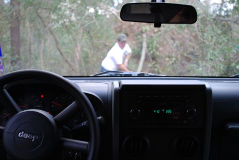 2008 Jeep Wrangler - View from inside a Jeep Wrangler looking out the windshield at a person bending over in the woods. The dashboard, steering wheel with the J…