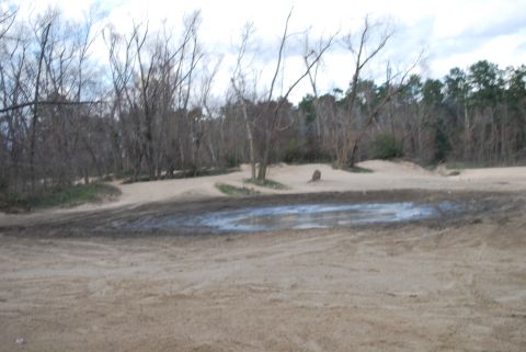 2008 Jeep Wrangler - A muddy puddle sits in a sandy area with bare trees in the background.