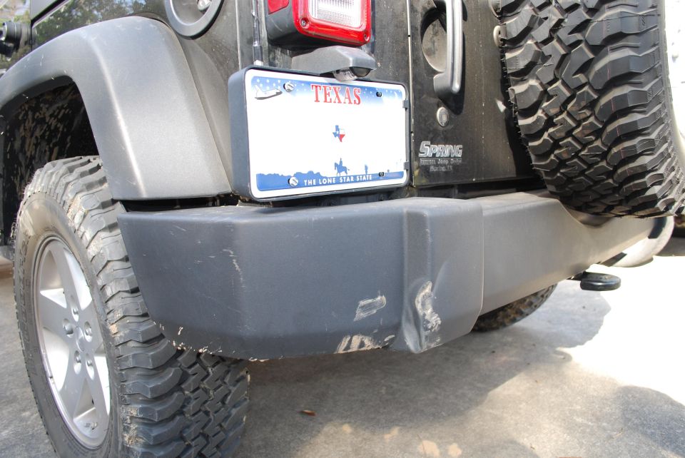 Rear bumper of a black Jeep Wrangler with a Texas license plate and scuff marks.