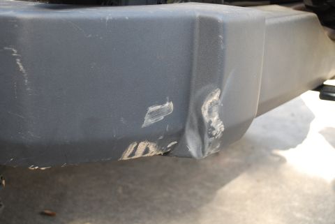 2008 Jeep Wrangler - A close-up view of a dented and scratched dark gray plastic bumper on a vehicle. There are scuff marks and some white residue on the damage…
