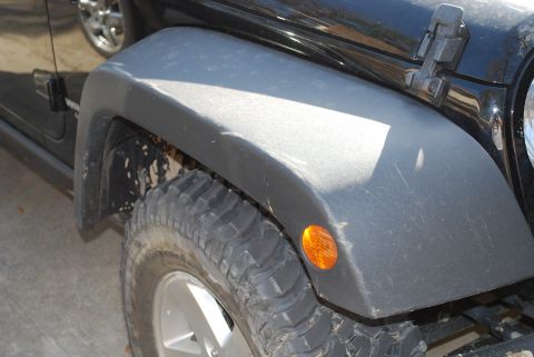 2008 Jeep Wrangler - A close-up view of the front fender and tire of a black Jeep Wrangler. The fender is made of black plastic and shows some dust and scratche…