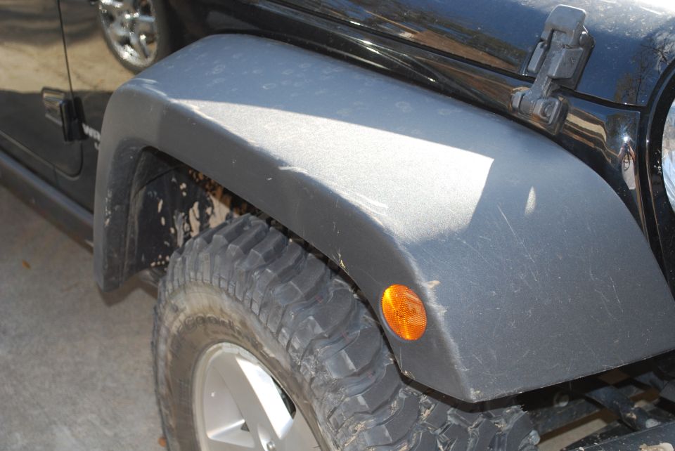 Black Jeep Wrangler front fender and tire with orange marker light.
