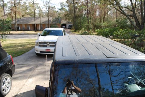2008 Jeep Wrangler - The roof of a black Jeep Wrangler is in the foreground, reflecting trees and a person holding a camera. A white Dodge Ram pickup truck is p…
