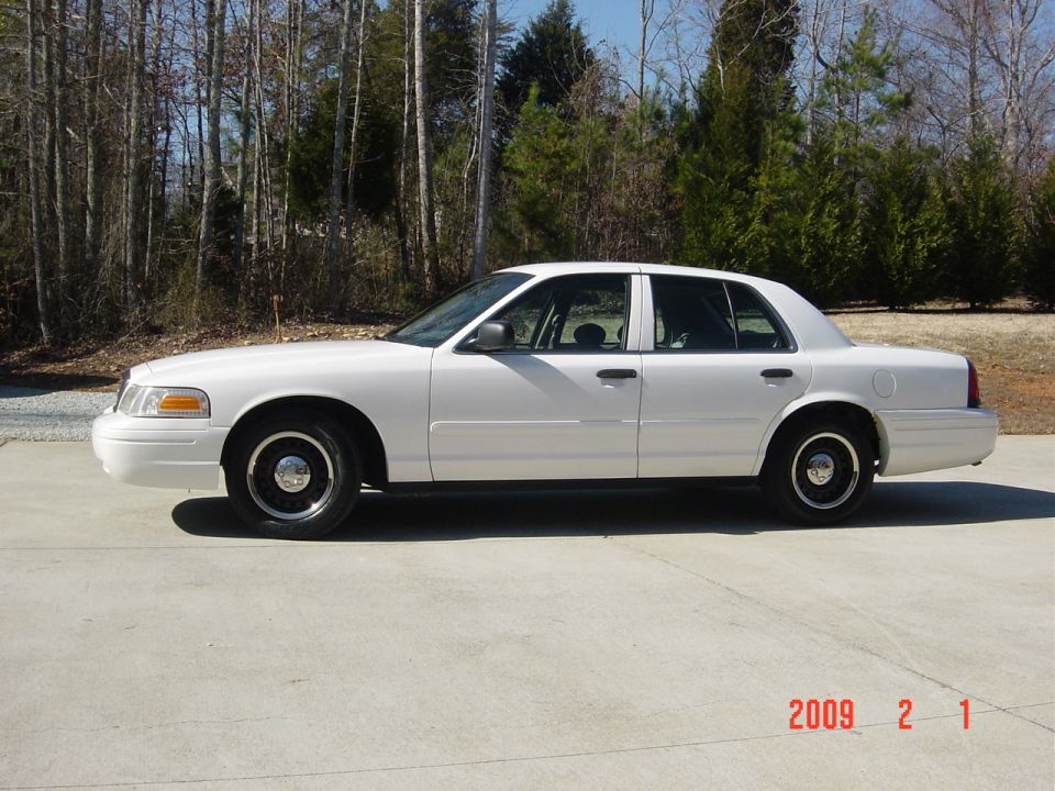 White 2002 Ford Crown Victoria sedan parked on concrete, side view.