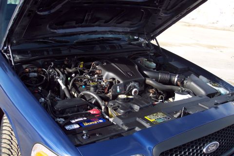 2001 Ford Crown Victoria - The engine bay of a blue 2001 Ford Crown Victoria is visible with the hood open, revealing the V8 engine and associated components.