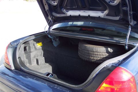 2001 Ford Crown Victoria - The trunk of a dark blue sedan, likely a 2001 Ford Crown Victoria, is open revealing a spare tire and trunk liner.