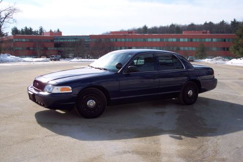 2001 Ford Crown Victoria - A dark blue Ford Crown Victoria is parked on a wet asphalt lot with snow visible in the background.