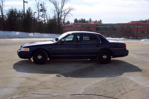 2001 Ford Crown Victoria - A dark blue 2001 Ford Crown Victoria sedan is parked on a lot with a building in the background.
