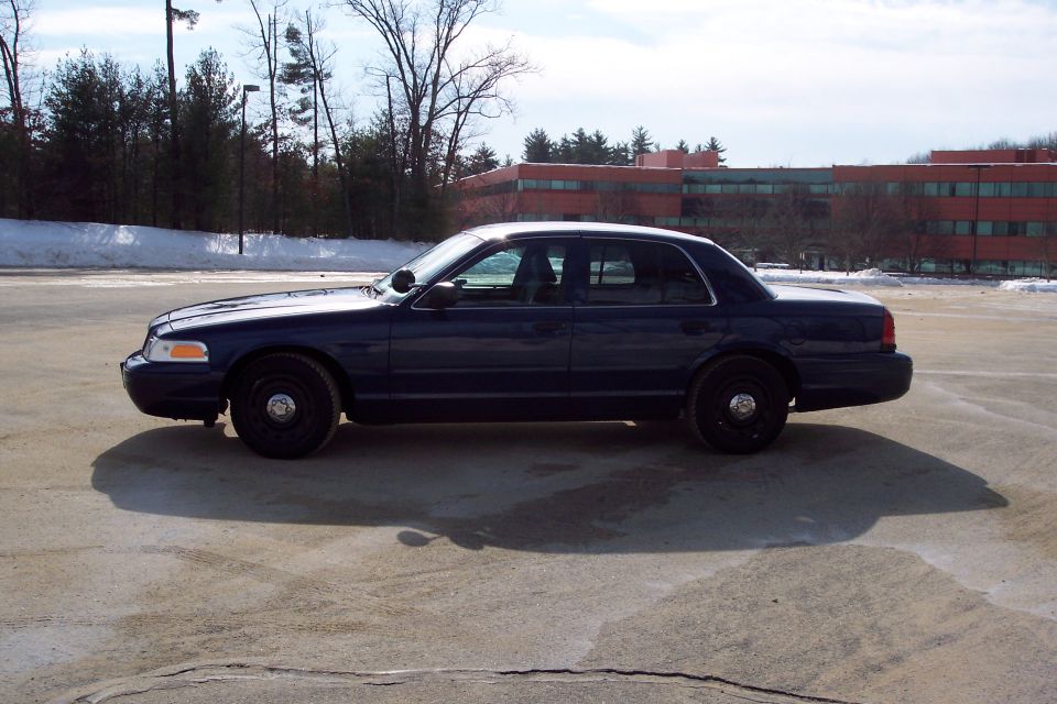 Dark blue 2001 Ford Crown Victoria sedan parked on cracked asphalt, side view