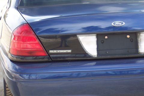 2001 Ford Crown Victoria - Rear view of a blue 2001 Ford Crown Victoria Police Interceptor, showing the taillight, Ford badge, and "Police Interceptor" emblem.