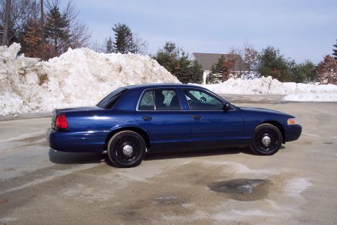 2001 Ford Crown Victoria - A blue 2001 Ford Crown Victoria sedan is parked on a lot with snow piles in the background.