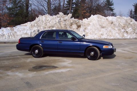 2001 Ford Crown Victoria - A blue 2001 Ford Crown Victoria sedan is parked on a lot with snow piles in the background.