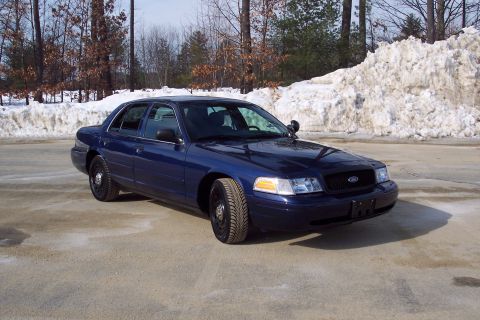2001 Ford Crown Victoria - A blue sedan is parked in front of a large pile of snow and bare trees.