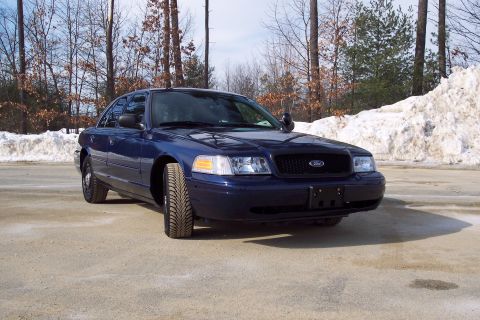 2001 Ford Crown Victoria - A dark blue 2001 Ford Crown Victoria sedan is parked on a dirt road with snow piles in the background.