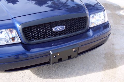 2001 Ford Crown Victoria - The front grille and headlights of a blue Ford Crown Victoria are visible, with a license plate bracket attached.