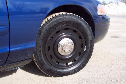 2001 Ford Crown Victoria - Front wheel and fender of a blue 2001 Ford Crown Victoria with a steel wheel cover.