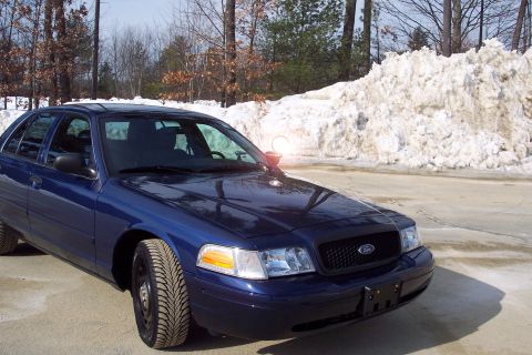 2001 Ford Crown Victoria - A blue 2001 Ford Crown Victoria is parked in front of a large snowbank, showing its front end and side profile.