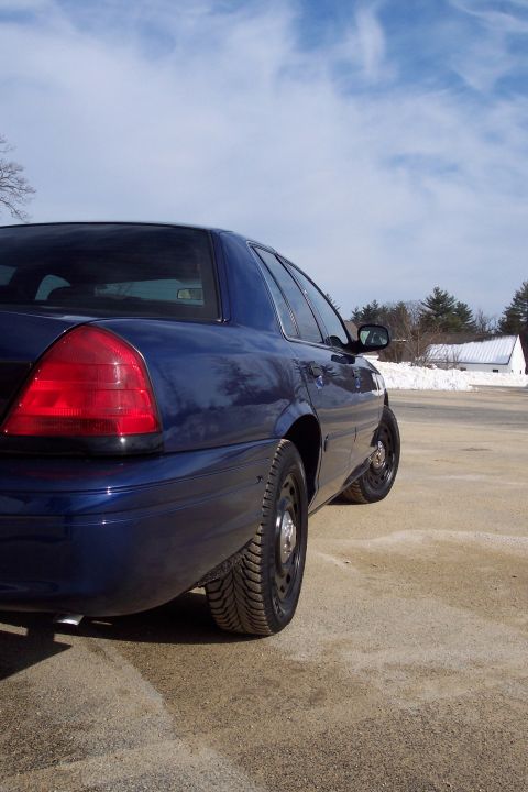 2001 Ford Crown Victoria - Rear quarter view of a dark blue sedan on a sunny day with a cloudy sky.