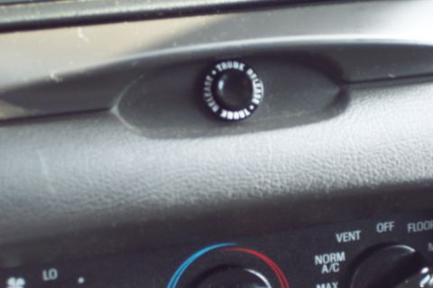 2001 Ford Crown Victoria - A close-up interior shot shows a black button with white text reading "TRUNK RELEASE" in a circular pattern. Below the button are climate c…