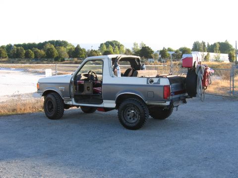 1991 Ford Bronco - A white 1991 Ford Bronco is seen from the front-right, with its doors off and kicking up dust.