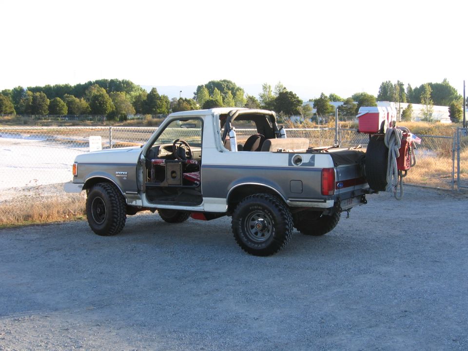 White 1991 Ford Bronco with doors removed, kicking up dust from a 3/4 front angle