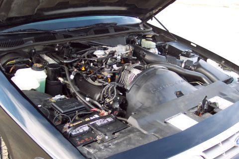 2001 Ford Crown Victoria - The engine bay of a dark colored vehicle, likely a Ford Crown Victoria, is shown with the hood open. Visible components include the engine,…