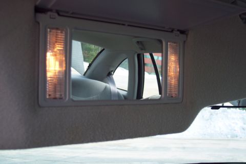 2001 Ford Crown Victoria - Sun visor vanity mirror with lights illuminated, reflecting the interior and exterior scene.