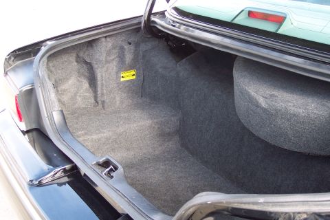 2001 Ford Crown Victoria - The spacious trunk of a Ford Crown Victoria, showing the carpeted interior and a spare tire. A yellow warning sticker is visible on the sid…