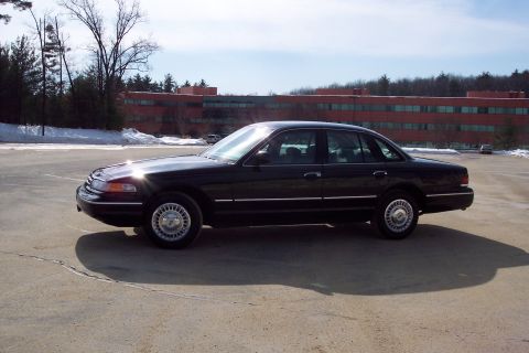 2001 Ford Crown Victoria - A black 2001 Ford Crown Victoria sedan is seen from the side in a parking lot with a building in the background.