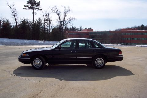 2001 Ford Crown Victoria - Side profile of a black 2001 Ford Crown Victoria sedan parked in a lot with a building in the background.