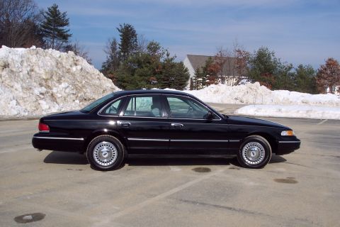 2001 Ford Crown Victoria - Side view of a black sedan parked outdoors with snowbanks and trees visible.