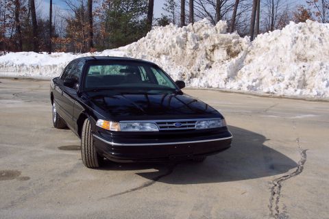 2001 Ford Crown Victoria - A black Ford Crown Victoria sits parked on a lot with snowbanks behind it.